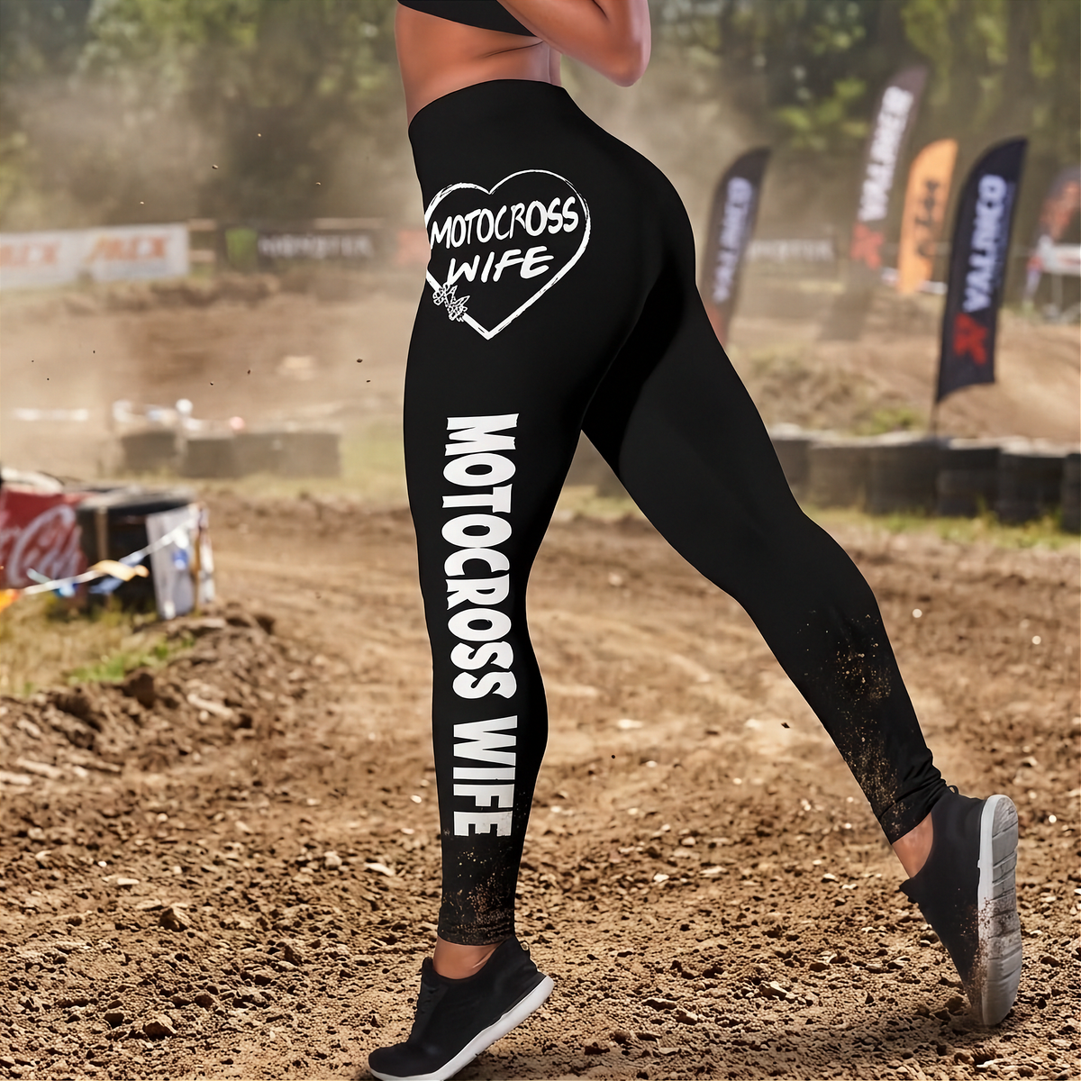 Black athletic leggings worn by a model on a dirt motocross track, featuring white text that reads 'MOTOCROSS WIFE' and a heart graphic with 'MOTOCROSS WIFE' inside.