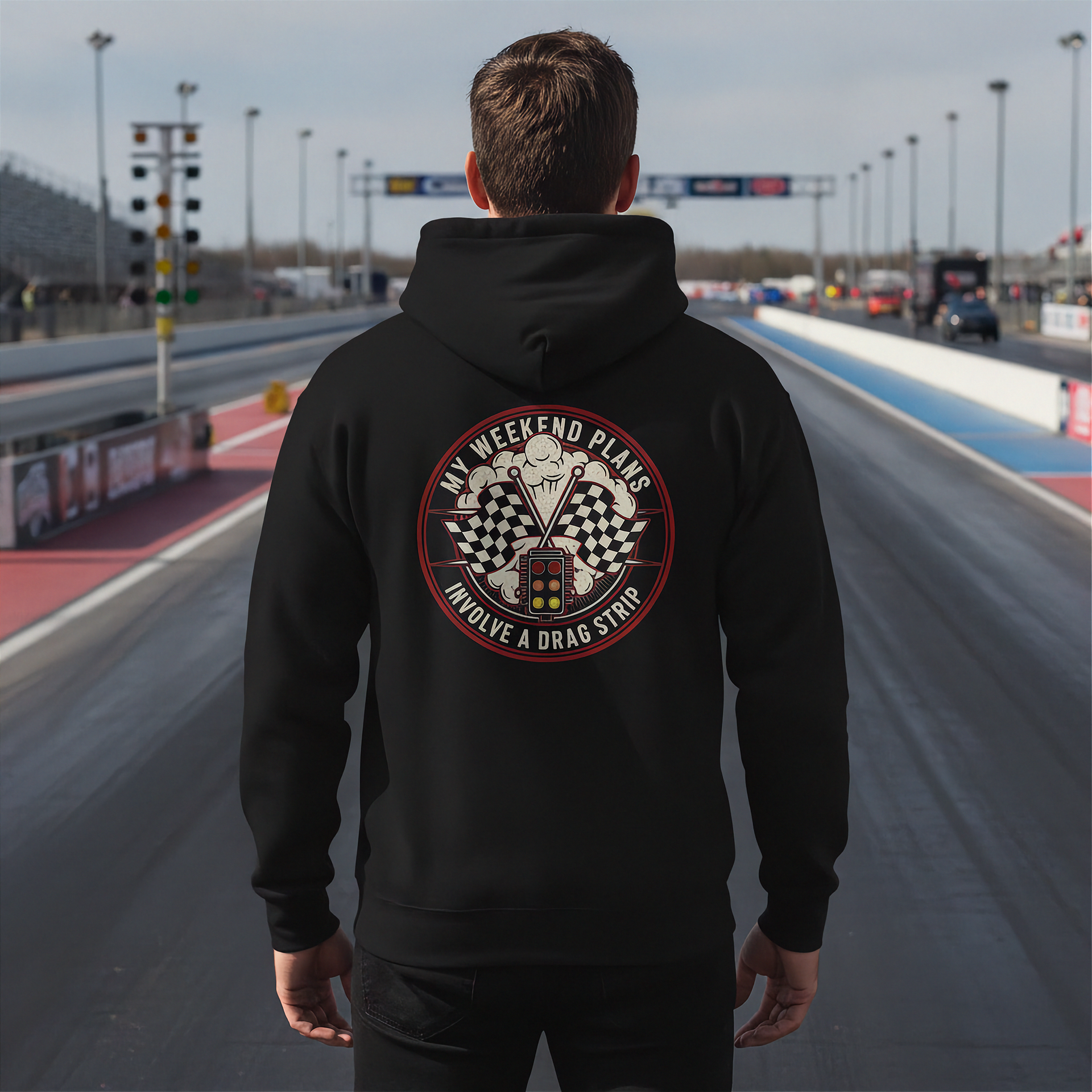 Man wearing a black hoodie with a graphic design on the back at a race track.