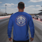 Man wearing a blue sweatshirt with a graphic design on the back at a drag strip.