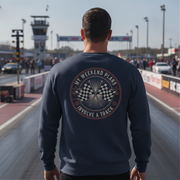 Man wearing a navy sweatshirt with a track-themed design at a race track.