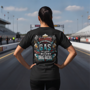 A woman stands on a racetrack from behind, wearing a black t-shirt with a colorful graphic on the back that reads 'ALCOHOL IS FOR DRINKING, NITRO IS DRAG RACING'.