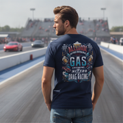 A man stands on a drag racetrack wearing a navy blue t-shirt with a large back graphic that reads 'ALCOHOL IS FOR DRINKING, NITRO IS DRAG RACING' with racing illustrations. The background shows blurred racetrack scenery with cars and grandstands.