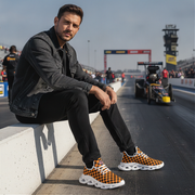 Man sitting on a race track wearing checkered shoes with racing cars in the background