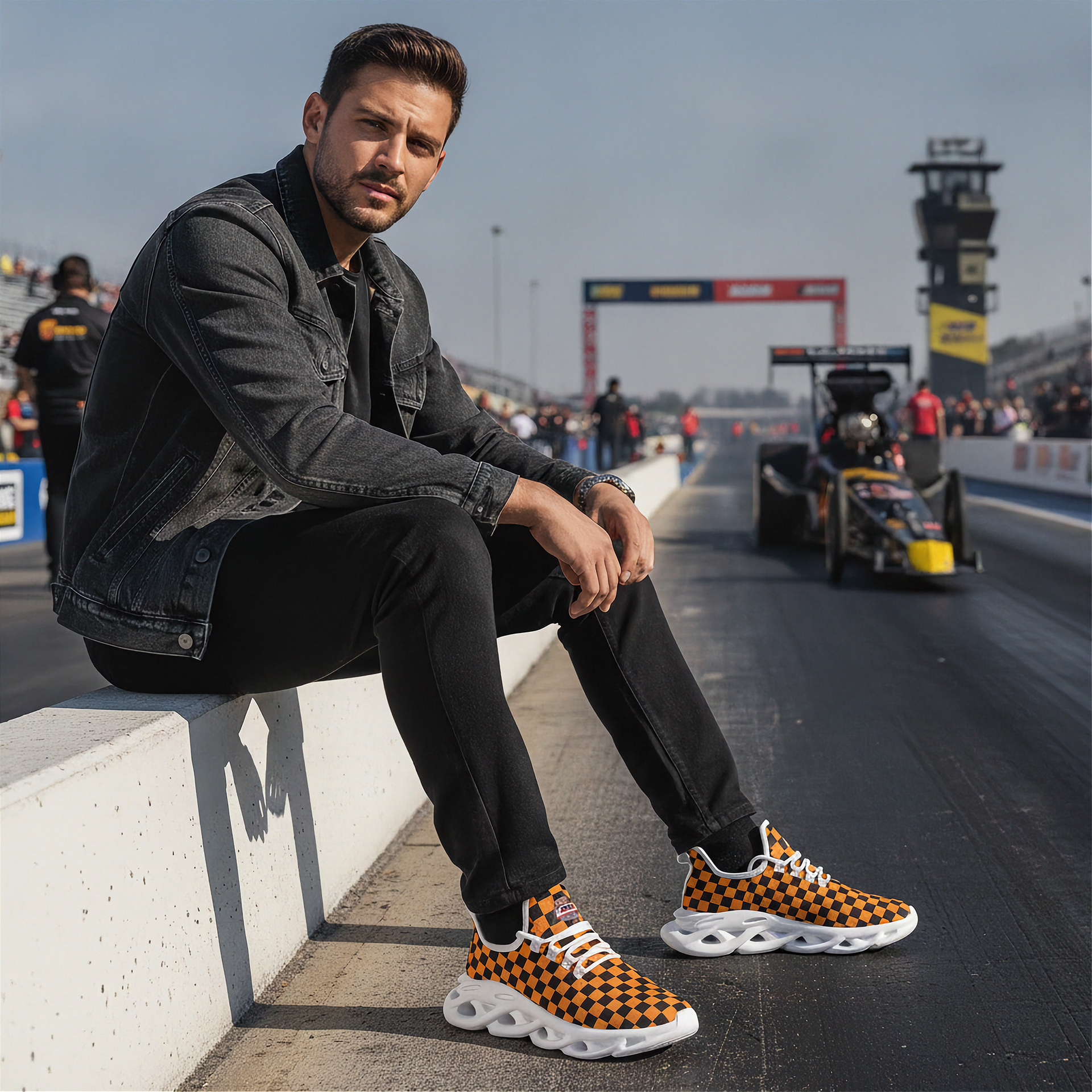 Man sitting on a race track wearing checkered shoes with racing cars in the background
