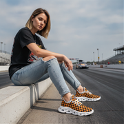 Woman sitting on a race track wearing black and orange checkered sneakers.
