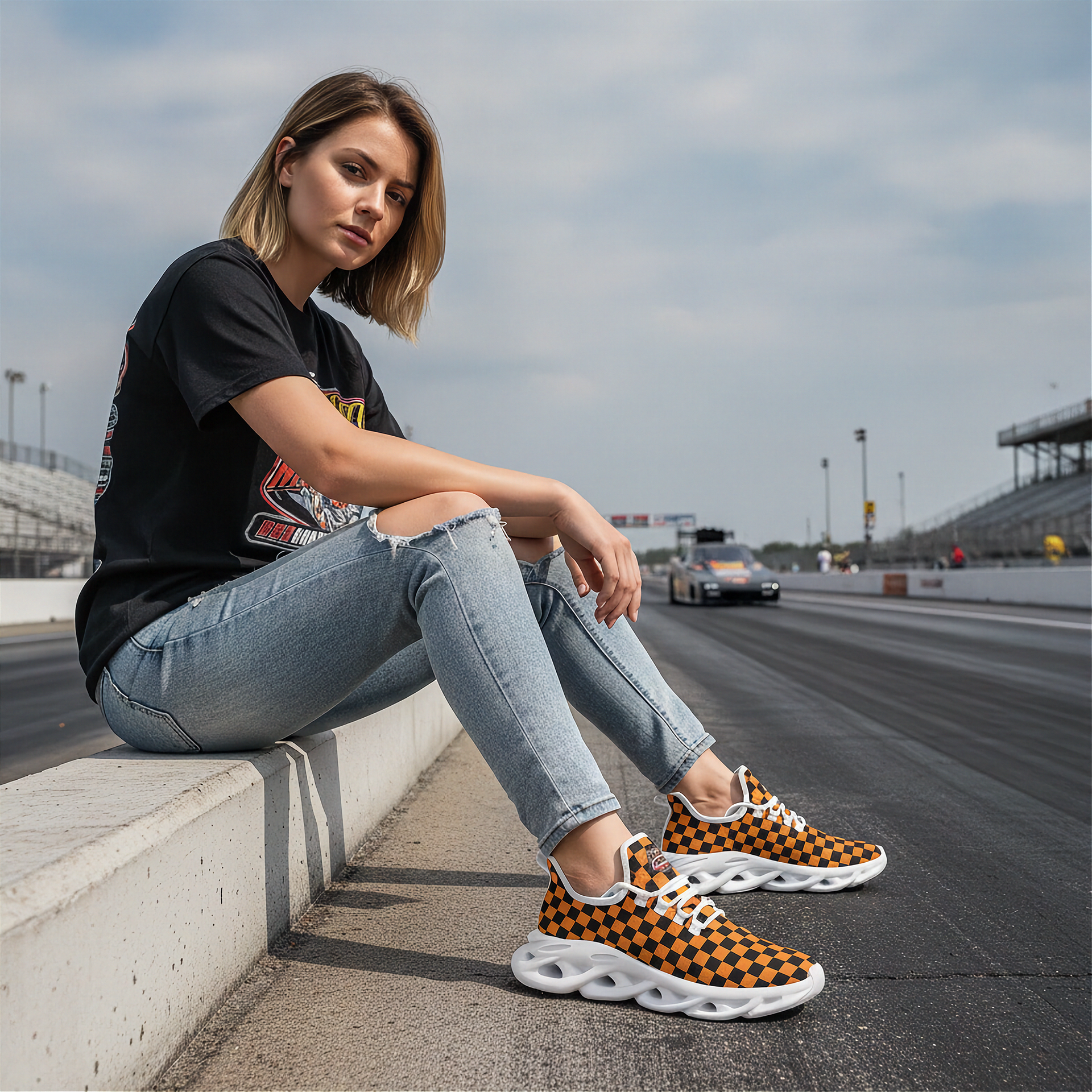 Woman sitting on a race track wearing black and orange checkered sneakers.