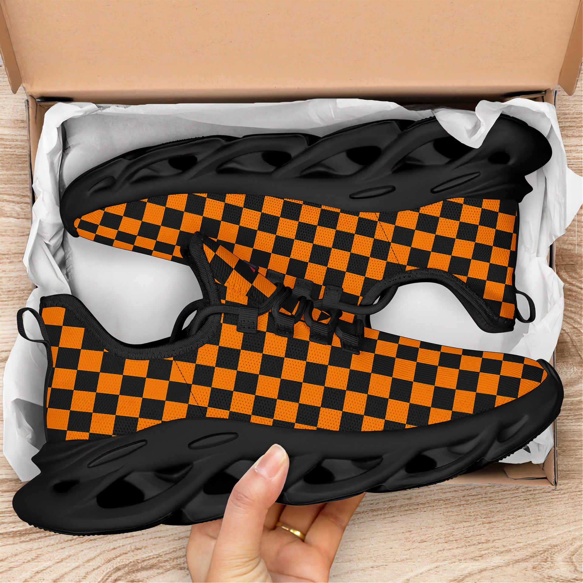 Orange and black checkered shoes in a box with a hand holding one shoe.