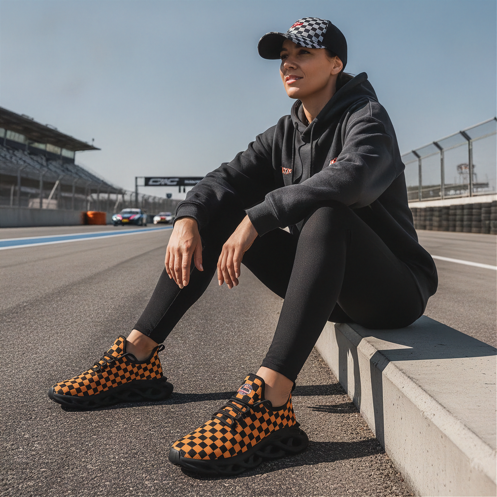 Man sitting on a race track wearing checkered shoes, cap, and hoodie.