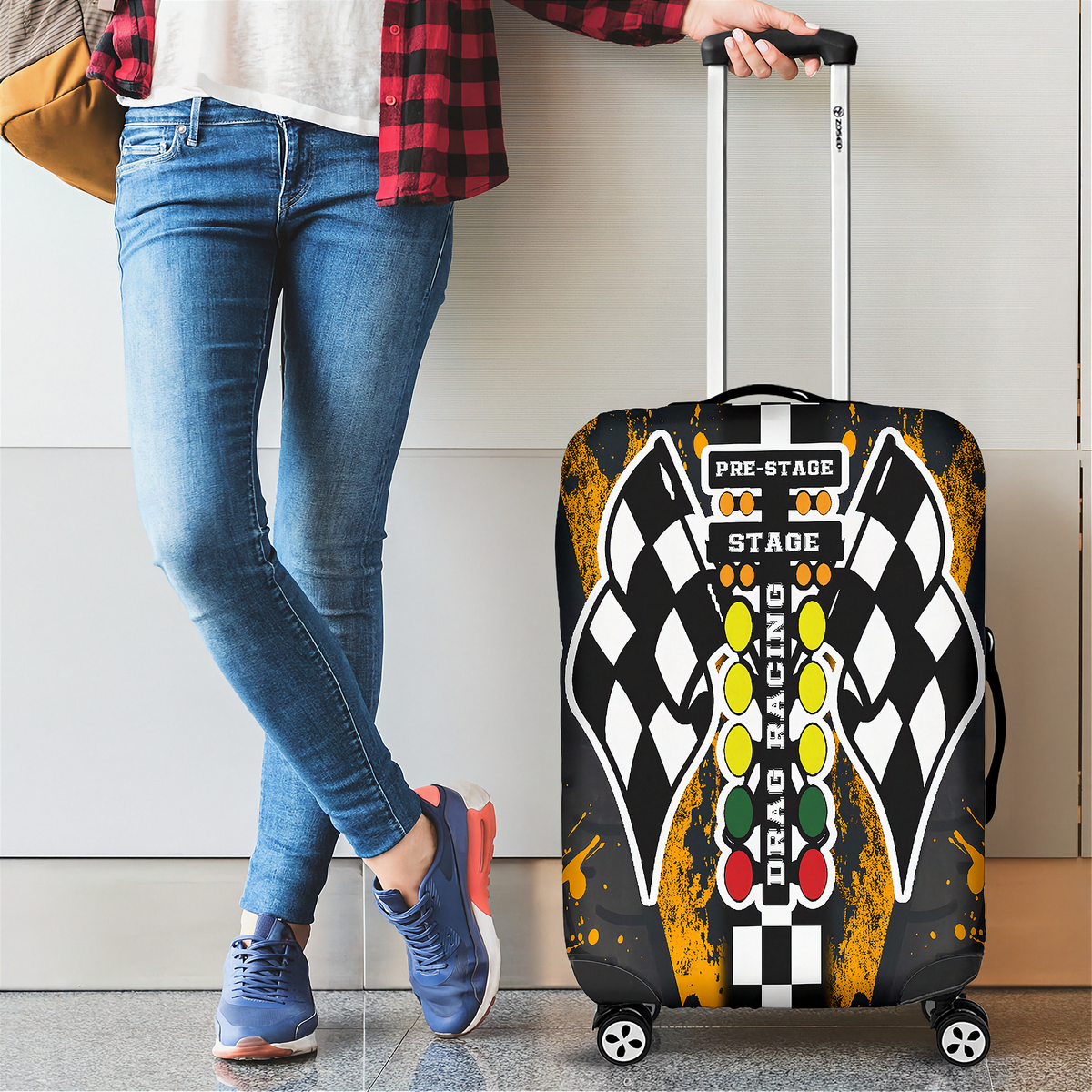 A person wearing blue jeans and a red plaid shirt stands beside a hard-shell rolling suitcase with a racing-themed cover design. The suitcase features a black and white checkered flag motif, yellow and red accents, and the words 'PRE-STAGE' and 'STAGE' on the front.