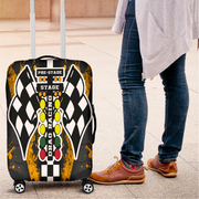A rolling suitcase with a racing-themed luggage cover is shown next to a person standing on a tiled floor. The cover features a black and white checkered wing design, yellow and green oval lights, and the words 'PRE-STAGE', 'STAGE', and 'DRAG RACING'.