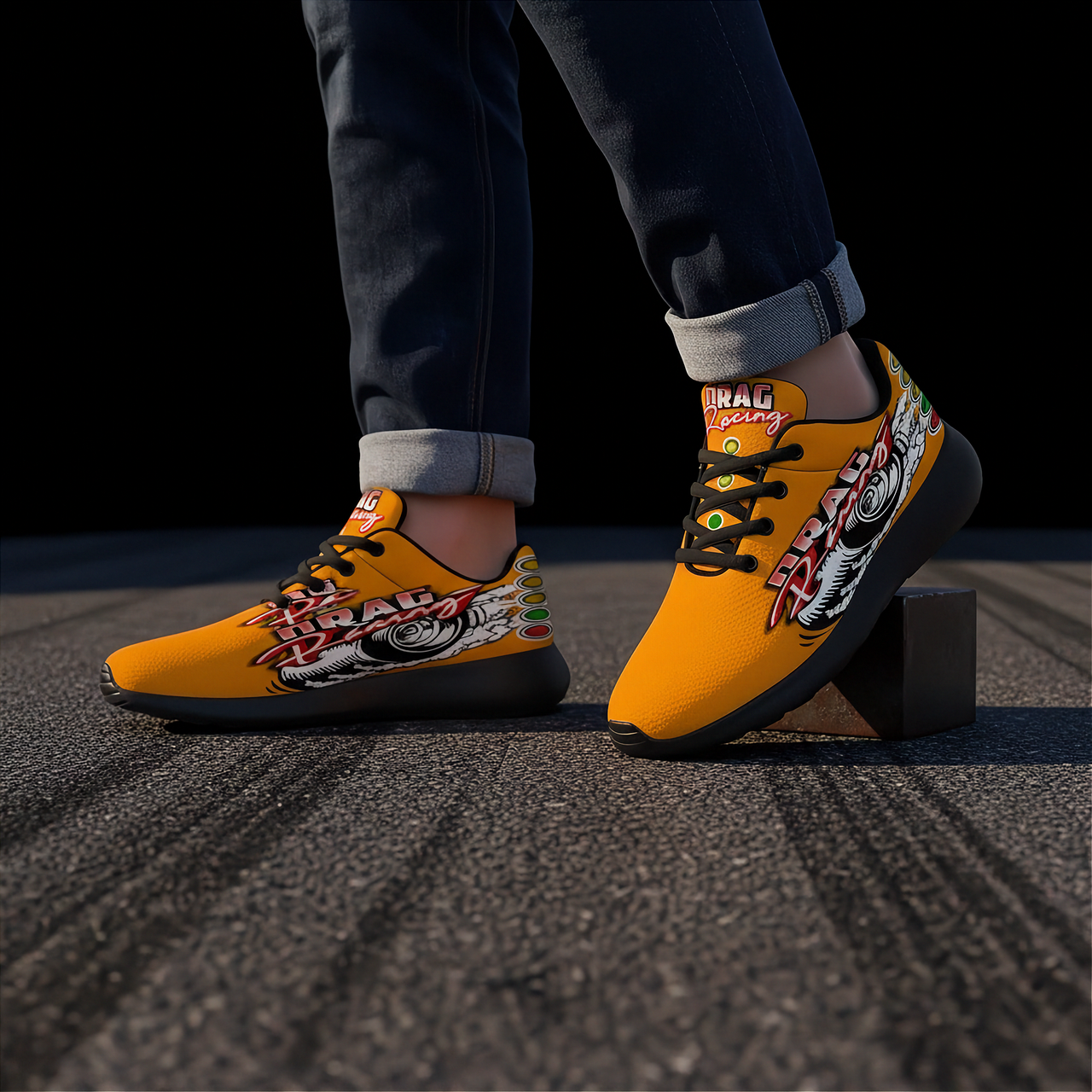 A person wearing bright yellow drag racing themed sneakers with graphic artwork , paired with dark cuffed jeans, standing on asphalt.