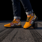 A person wearing bright yellow drag racing themed sneakers with graphic artwork , paired with dark cuffed jeans, standing on asphalt.