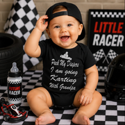 Baby wearing a black onesie with racing-themed text, sitting on a checkered floor with racing decor.