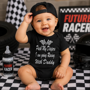 Baby wearing a black onesie with racing-themed text, sitting on a checkered floor with racing-themed decor.