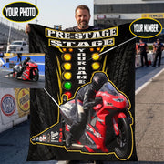 A man stands on a racetrack holding a large custom motorcycle-themed banner or poster. The banner has a black background with yellow and white text reading 'PRE-STAGE STAGE', a vertical 'YOUR NAME' field, colored light bar graphics, and a large red motorcycle with a rider illustration.