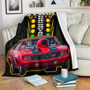 A black throw blanket draped over a cream sofa in a living room, featuring a printed design of a red muscle car in front of a yellow racing light sign with the words 'DRAG RACING'.