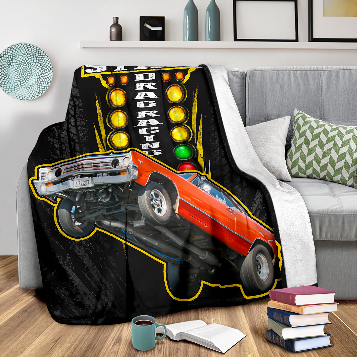 A black throw blanket draped over a gray sofa in a living room setting, featuring a graphic print of an orange drag racing car and a yellow racing light panel.