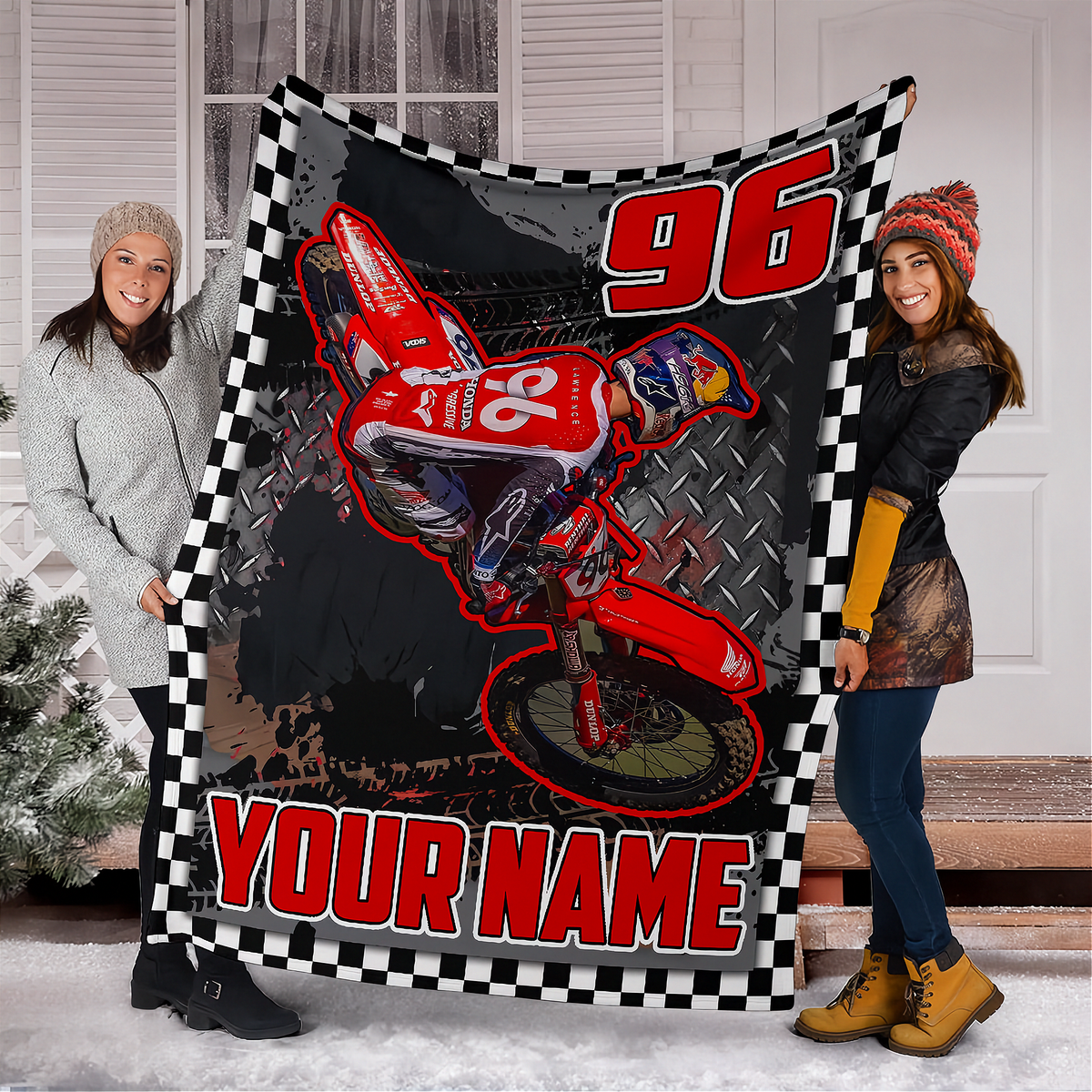 A custom motocross blanket featuring a red dirt bike graphic, the number 96, and 'YOUR NAME' text, held up by two smiling women in front of a white door.