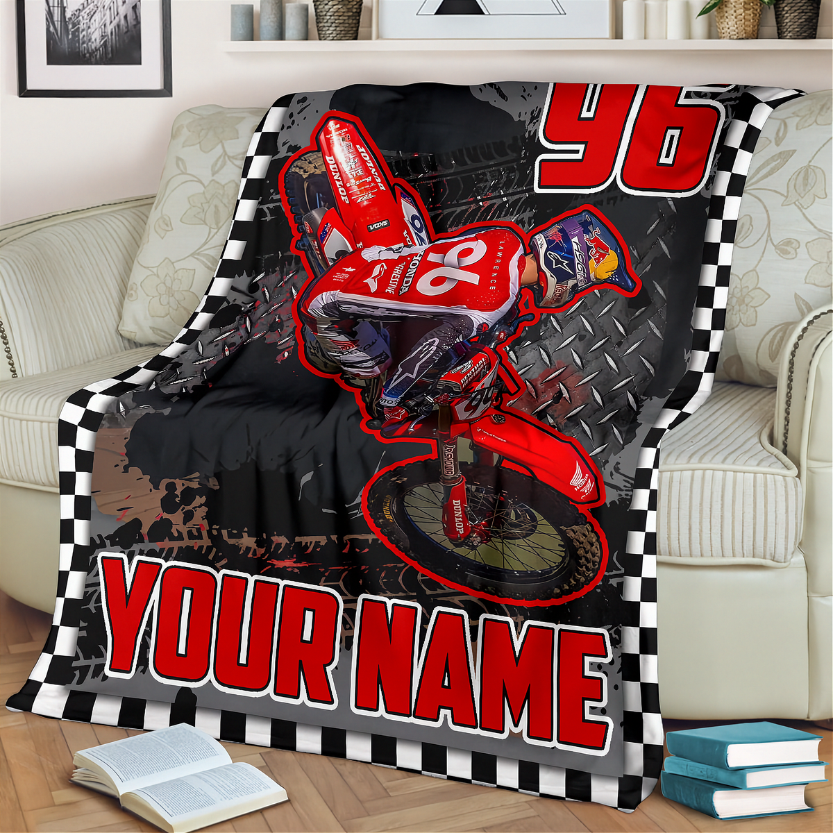 A custom printed blanket draped over a beige sofa in a living room setting. The blanket features a red dirt bike racer graphic with the number 96, a black and white checkered border, and the text 'YOUR NAME' in bold red letters.