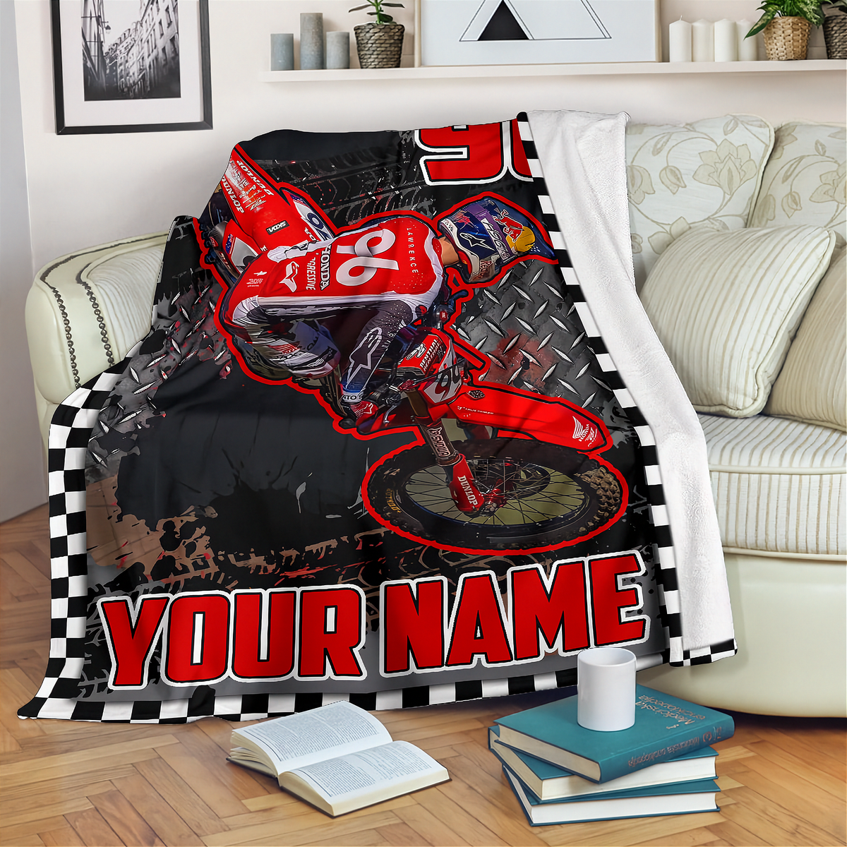 A custom printed blanket draped over a sofa in a living room setting. The blanket features a red dirt bike racer graphic on a black and white checkered background with the text 'YOUR NAME' in bold red letters.
