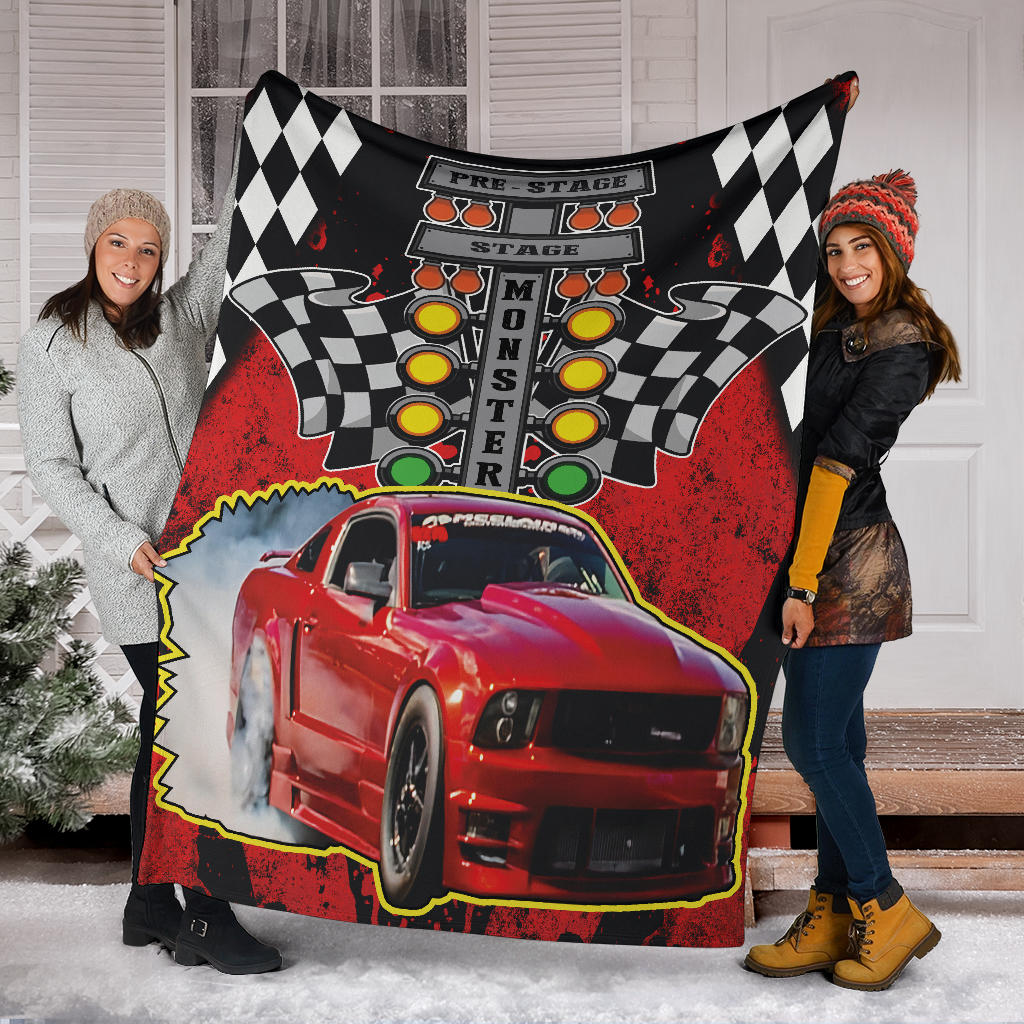 Two women holding a personalized red Mustang drag racing blanket with sample name MONSTER outside a house in the snow.