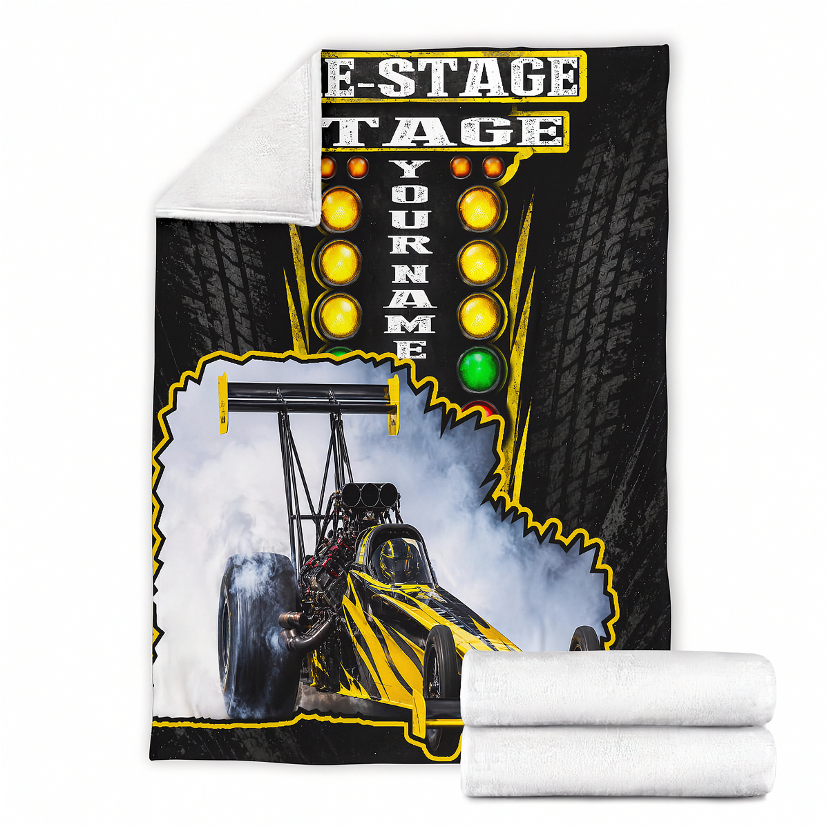 A custom printed fleece blanket featuring a drag racing graphic with a yellow and black dragster, tire tracks, and a marquee-style light sign with the text 'E-STAGE TAGE YOUR NAME'. A white sherpa lining is visible on the reverse side, and two folded white blankets are shown at the bottom right.
