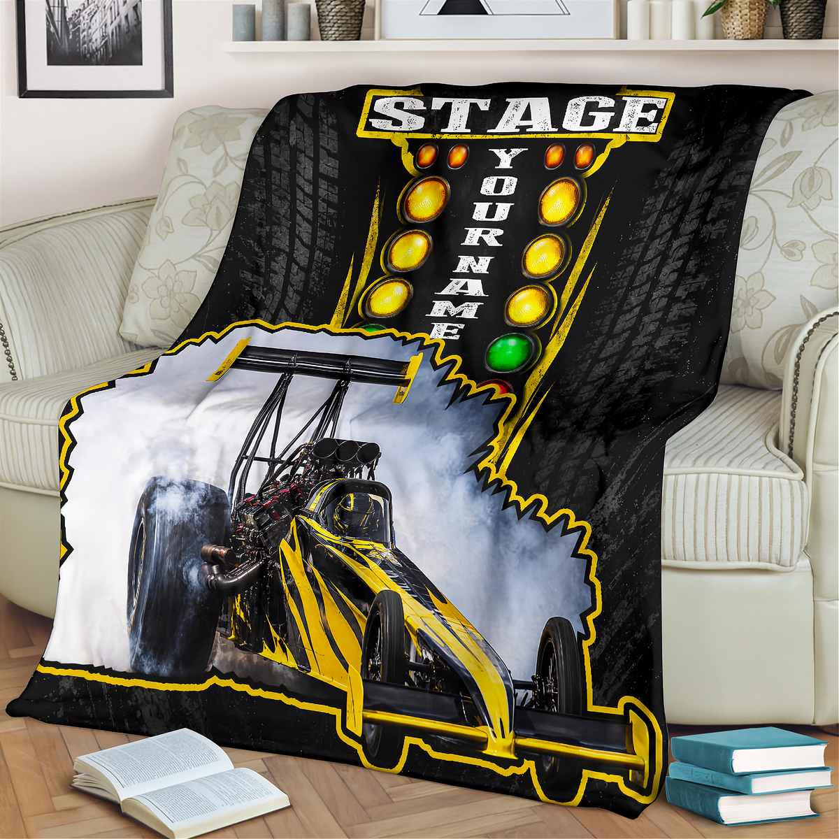 A custom printed fleece blanket draped over a light beige sofa in a living room setting. The blanket features a black and yellow drag racing theme with a graphic of a race car smoking tires, a yellow 'STAGE YOUR NAME' light bar design, and a white smoke border.