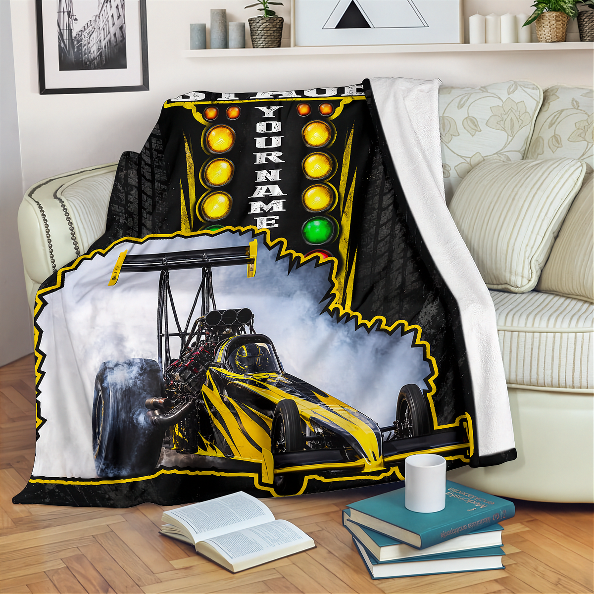 A custom printed fleece throw blanket draped over a cream sofa in a living room setting. The blanket features a black and yellow drag racing theme, with a large graphic of a yellow and black drag racer in smoke, a vertical 'YOUR NAME' text field, and yellow light bulbs.