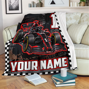 A custom fleece throw blanket featuring a black and red Formula 1 race car design, a large number 1, and 'YOUR NAME' text, draped over a light beige sofa in a living room setting.