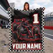 A woman stands on a racetrack holding a large customizable fleece blanket. The blanket features a black and red Formula 1 race car, a large white number 1, and a black-and-white checkered border, with the text 'YOUR NAME' at the bottom.