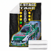 A custom printed fleece blanket featuring a green and white Ford race truck on a black tire-pattern background with stage lights and the text 'RACE-STAGE YOUR NAME'. A white sherpa lining is visible on the folded top corner, and two rolled white towels are shown in front on a plain white background.