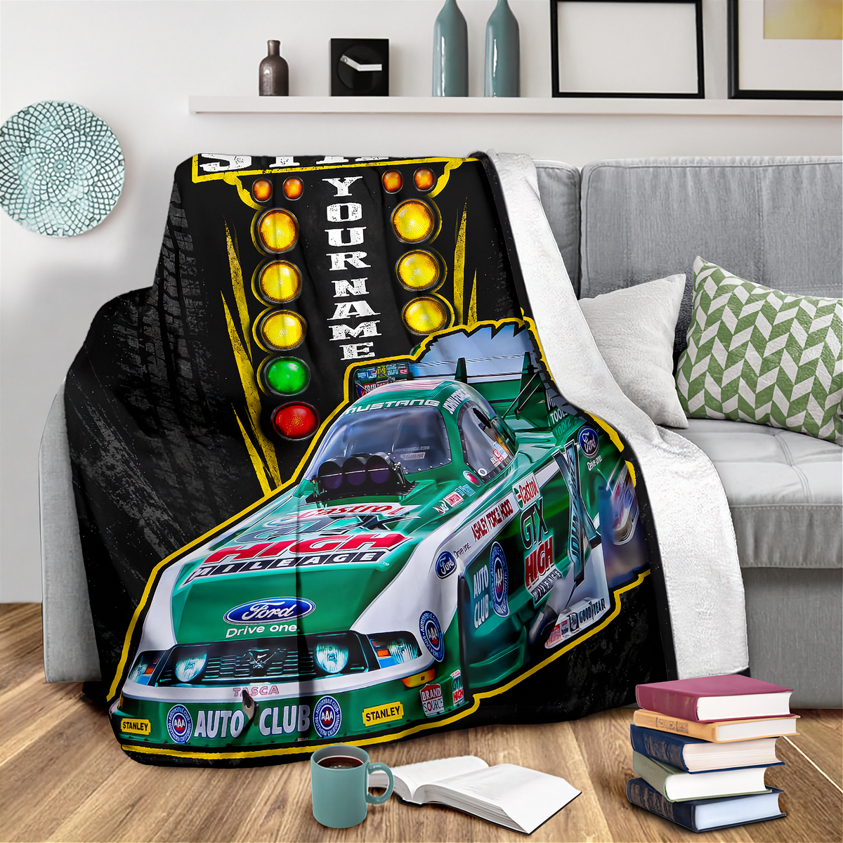 A custom printed fleece blanket draped over a gray sofa in a living room setting. The blanket features a green and white Ford race car with '2000 AUTO CLUB' and 'Ford' branding, alongside a black background with yellow, orange, and red traffic light graphics and the text 'YOUR NAME'.