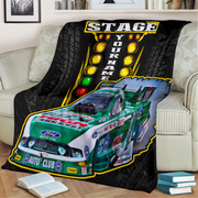 A custom printed fleece throw blanket draped over a beige sofa in a living room setting. The blanket features a green and white Ford race car, a yellow 'STAGE YOUR NAME' light bar graphic, and tire tracks on a black background.
