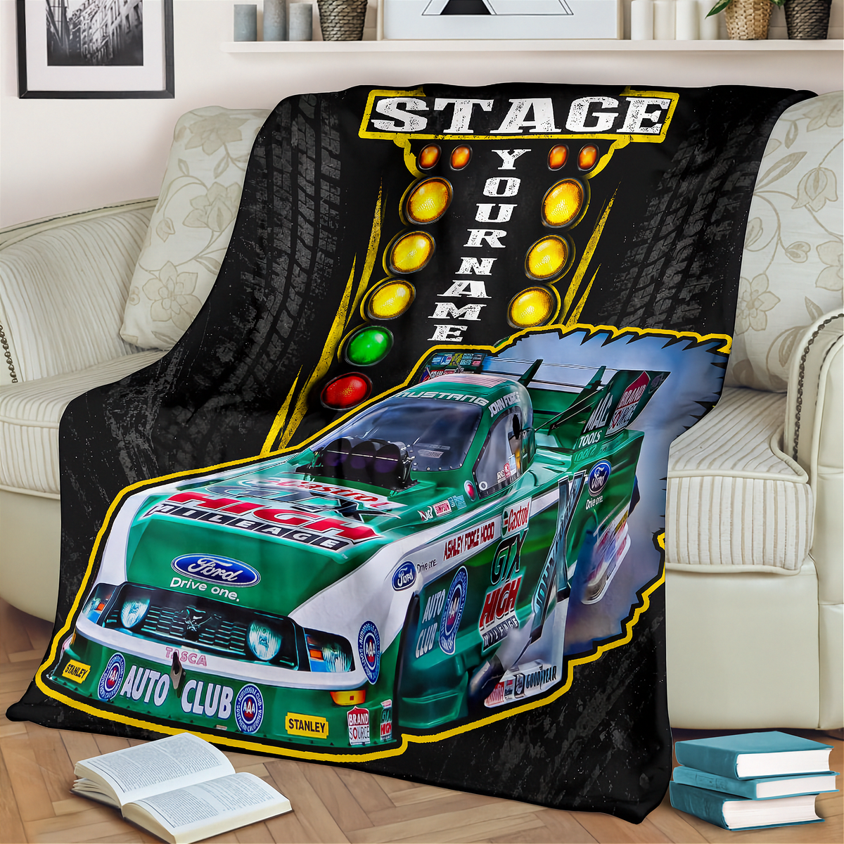 A custom printed fleece throw blanket draped over a beige sofa in a living room setting. The blanket features a green and white Ford race car, a yellow 'STAGE YOUR NAME' light bar graphic, and tire tracks on a black background.
