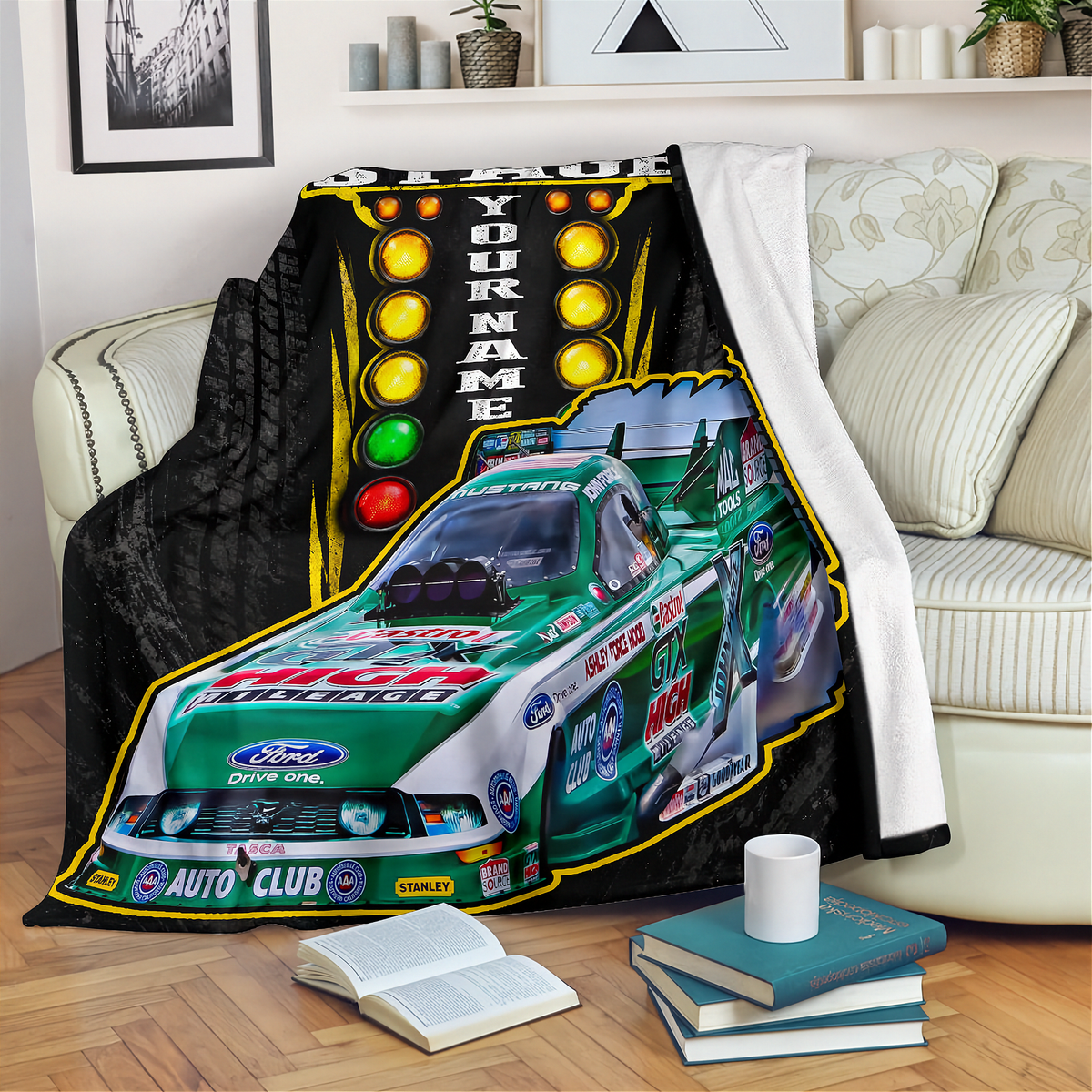 A custom racing-themed fleece throw blanket draped over a cream-colored sofa in a living room setting. The blanket features a green and white Ford race car with racing decals, a black background, and a vertical light bar graphic with the text 'YOUR NAME' and 'SPARE THE LIGHTS'.