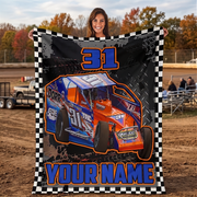 A woman stands outdoors holding up a large custom race blanket. The blanket features a black and white checkered border, a graphic of a blue and orange race car with the number 31, and the text '31' at the top and 'YOUR NAME' at the bottom.