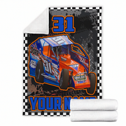 A custom printed fleece blanket featuring a blue and orange race car with the number 31, a black-and-white checkered border, and a white sherpa lining. Two rolled white towels are shown in front of the blanket on a plain white background.