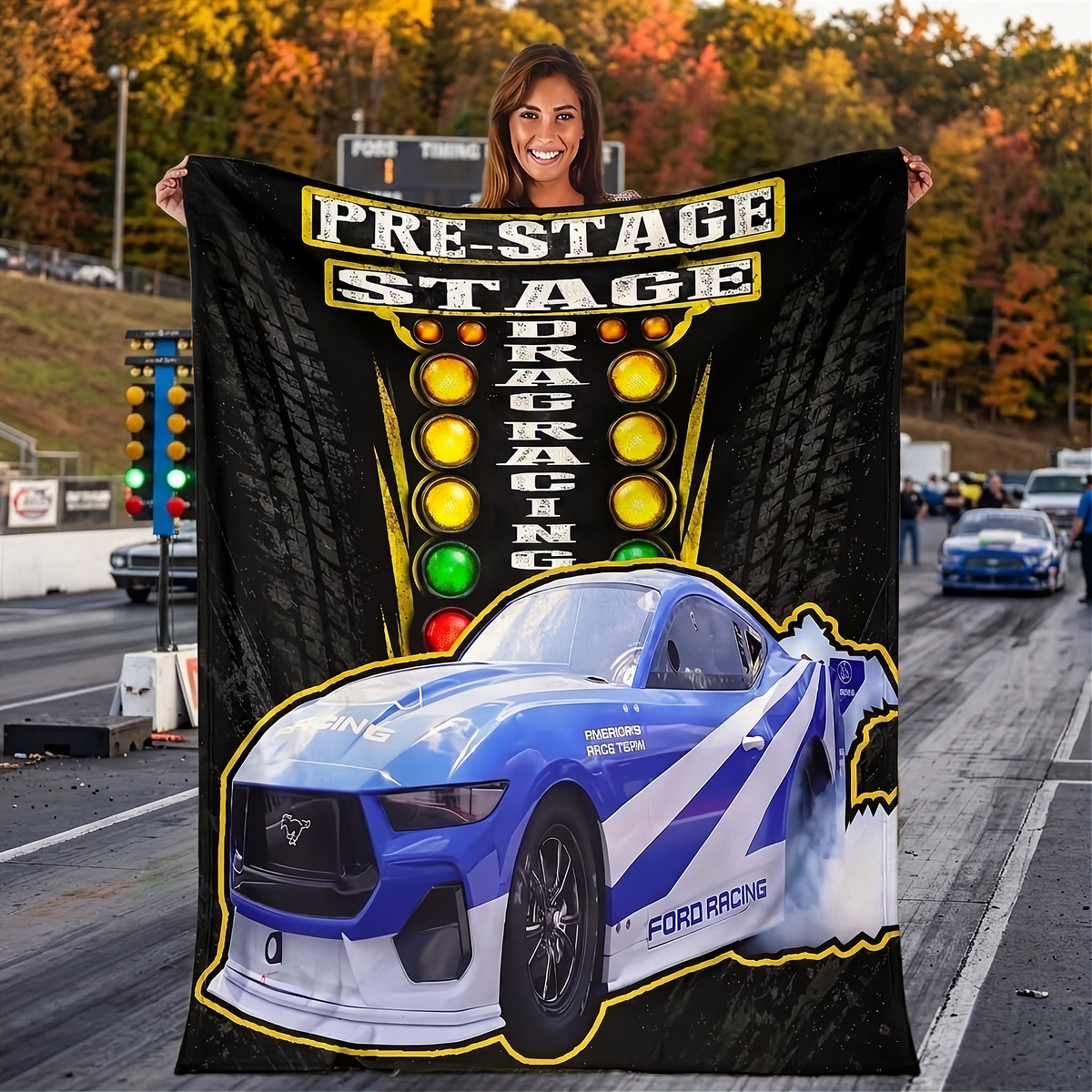A woman stands on a racetrack holding a large printed blanket or poster. The product shows a blue and white Ford racing car with 'FORD RACING' text, a yellow pre-stage lighting graphic, and tire patterns on a black background.