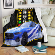 A fleece throw blanket draped over a cream sofa in a living room setting, featuring a printed design of a blue Ford Mustang race car in front of a black track lighting grid background.