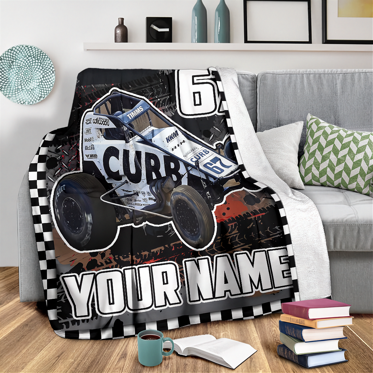 A custom printed blanket featuring a dirt truck race car graphic with the number 6 and the name 'CUBB' on a couch in a living room setting. The blanket includes a checkered border and the text 'YOUR NAME' for personalization.