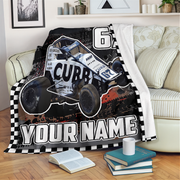 A personalized racing blanket draped over a sofa in a living room setting. The blanket features a black and white checkered border, a graphic of a white and blue Non Wing race car with 'CUBB' and number '62' printed on it, and the text 'YOUR NAME' in bold white letters.