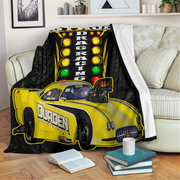 A black and yellow drag racing themed blanket draped over a cream sofa in a living room setting, featuring a yellow race car and a vertical light bar graphic.