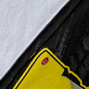 Close-up detail of a bright yellow sticker or decal with a black outline, placed over a black textured surface with a white textured area at the top.