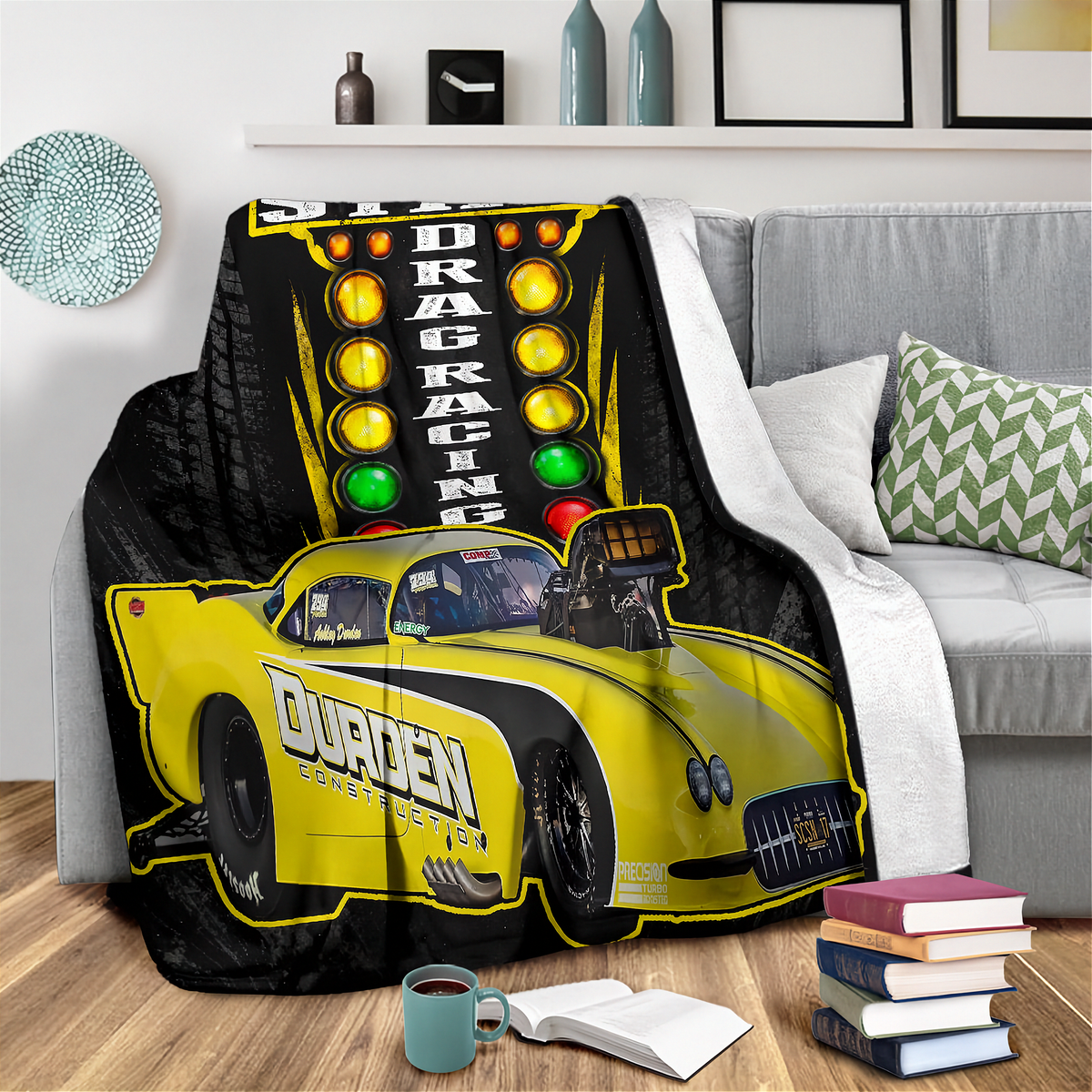 A yellow and black drag racing themed blanket draped over a gray sofa in a living room setting, featuring a race track light graphic and a yellow drag racer car with 'Duren' branding.
