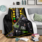 A black fleece throw blanket featuring a racing motorcycle and drag racing graphic, draped over a gray sofa in a living room setting.