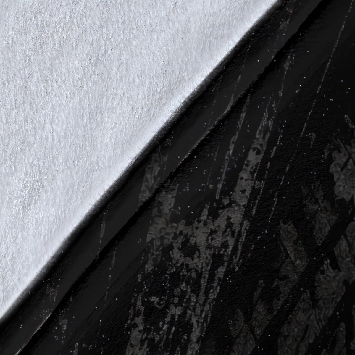 A close-up of a black textured surface with a diagonal split showing a white textured side.
