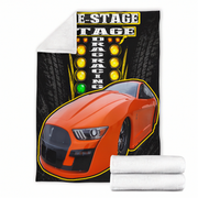 A fleece throw blanket featuring a graphic print of an orange drag racing car in front of a tire wall and marquee lights. The blanket is shown partially unfolded to reveal a white sherpa lining, with two folded white blankets stacked at the bottom right on a plain white background.