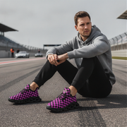 Man sitting on a race track wearing gray hoodie and black pants with pink checkered shoes.