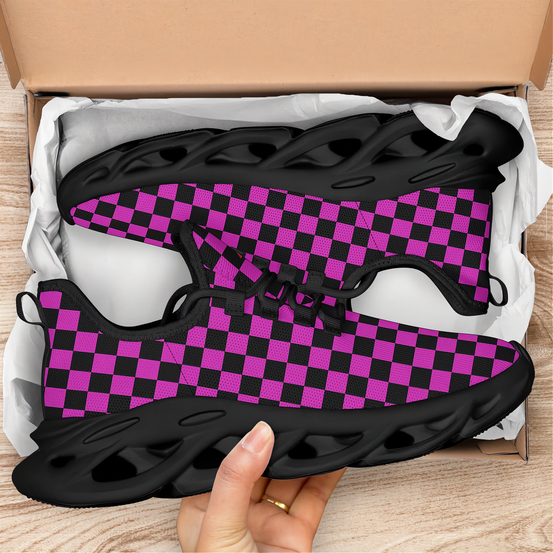 Black and purple checkered shoes in an open box with a hand holding one shoe.