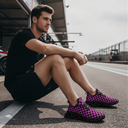 Man sitting on a race track wearing black and purple checkered shoes.